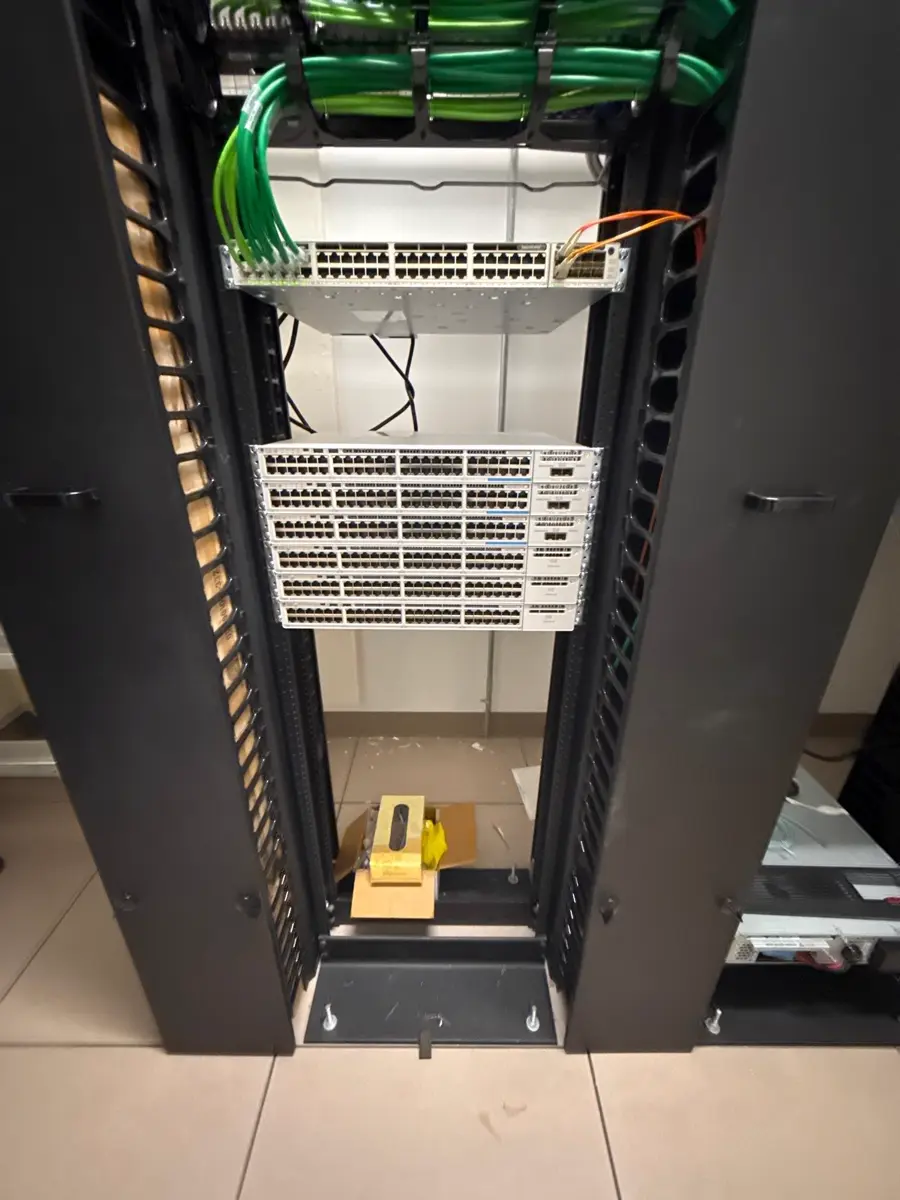 Open rack: a 48-port patch panel with green patch cables over six rack-mounted switches.