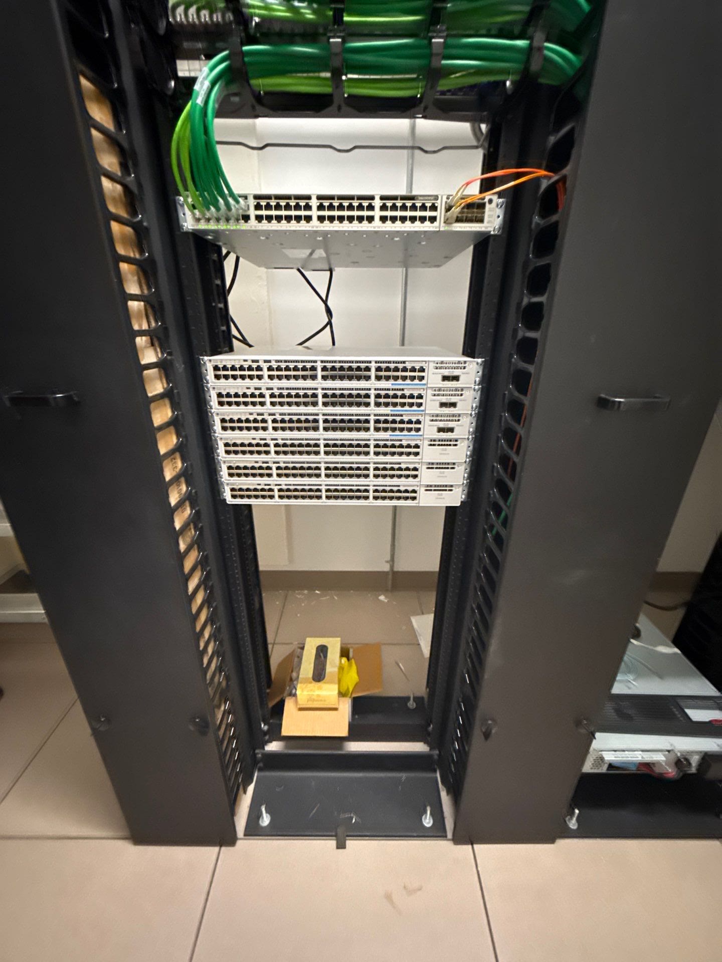 Open equipment rack: 48-port patch panel with green patch cables over six rack-mounted switches.