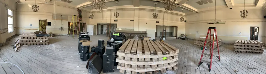 An empty ballroom mid-renovation, chandeliers and bare subfloor.