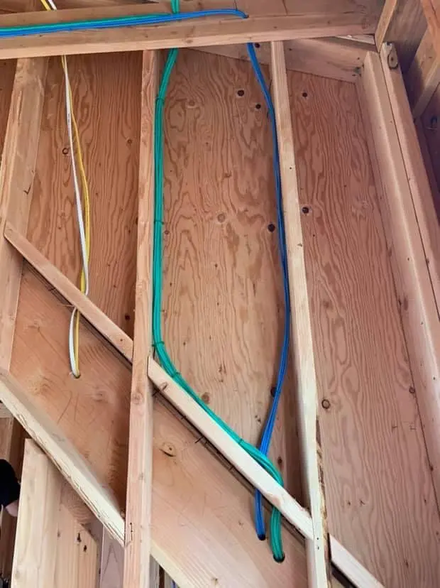 Green and blue low-voltage cable dressed down a stud bay in an unfinished commercial wall.
