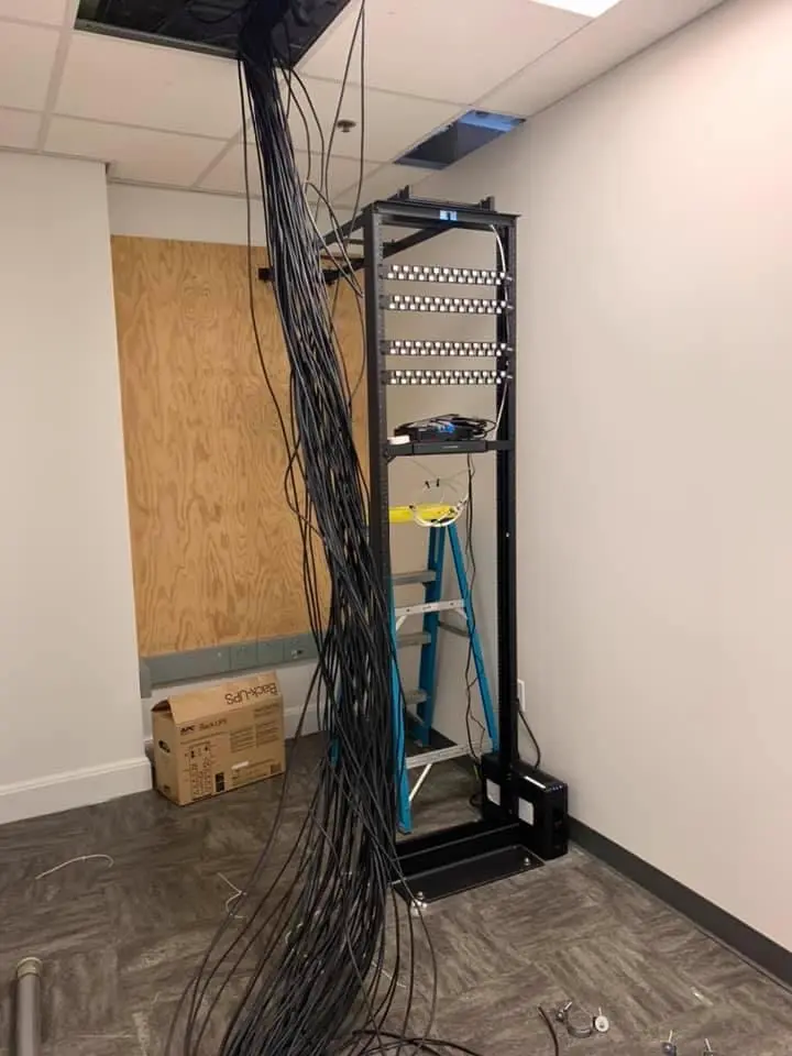Open server rack with patch panels, a stepladder, and a cable bundle dropping from the ceiling.