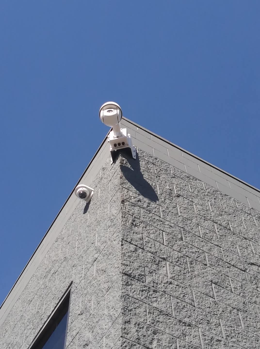 Two dome and PTZ security cameras mounted at a building roofline against blue sky