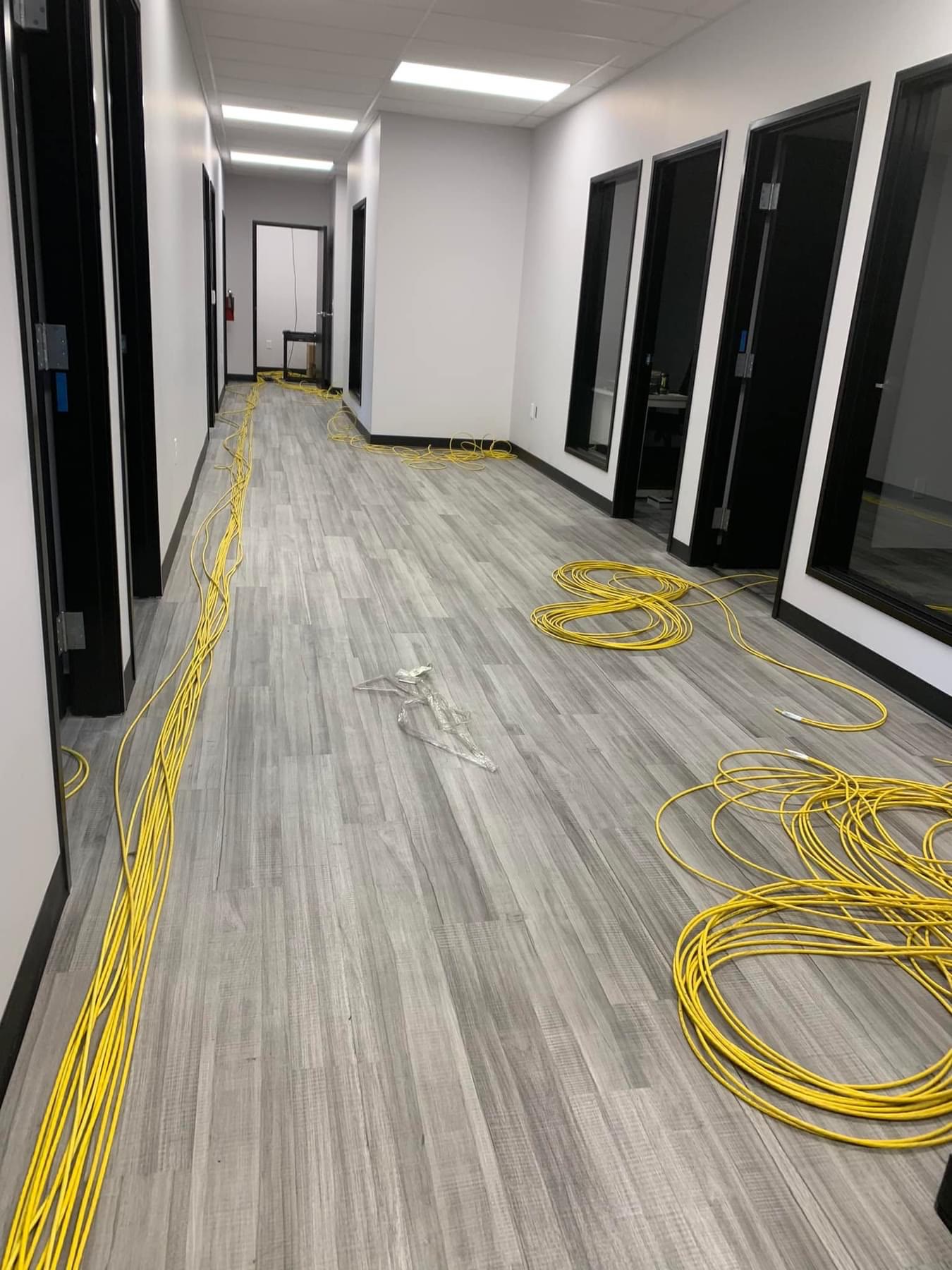 Office hallway mid-cabling: coiled yellow patch cable on the floor, glass-front offices along the hall.