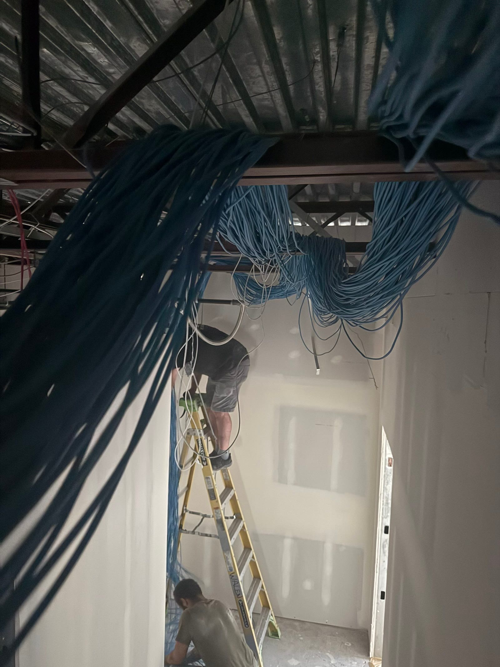 Cable being run through a ceiling plenum, one crew member on a ladder