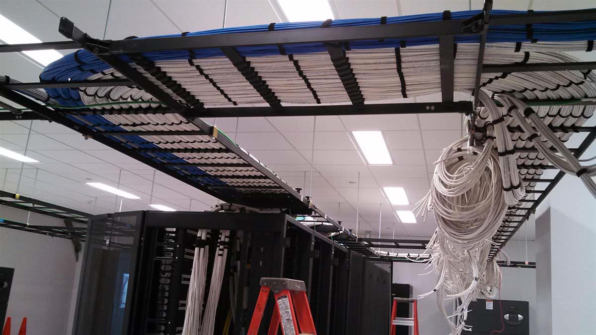 An overhead cable tray packed with combed Cat cable above open server racks
