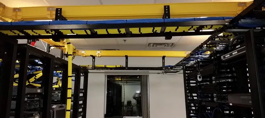 Wide interior data-room shot: yellow cable ladder trays feeding server racks on both sides.