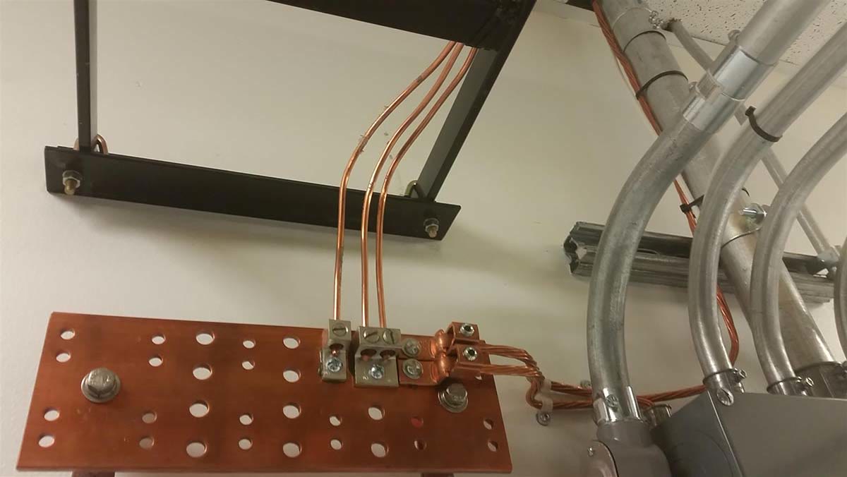 Copper grounding bus bar in an equipment rack, with EMT conduit overhead.