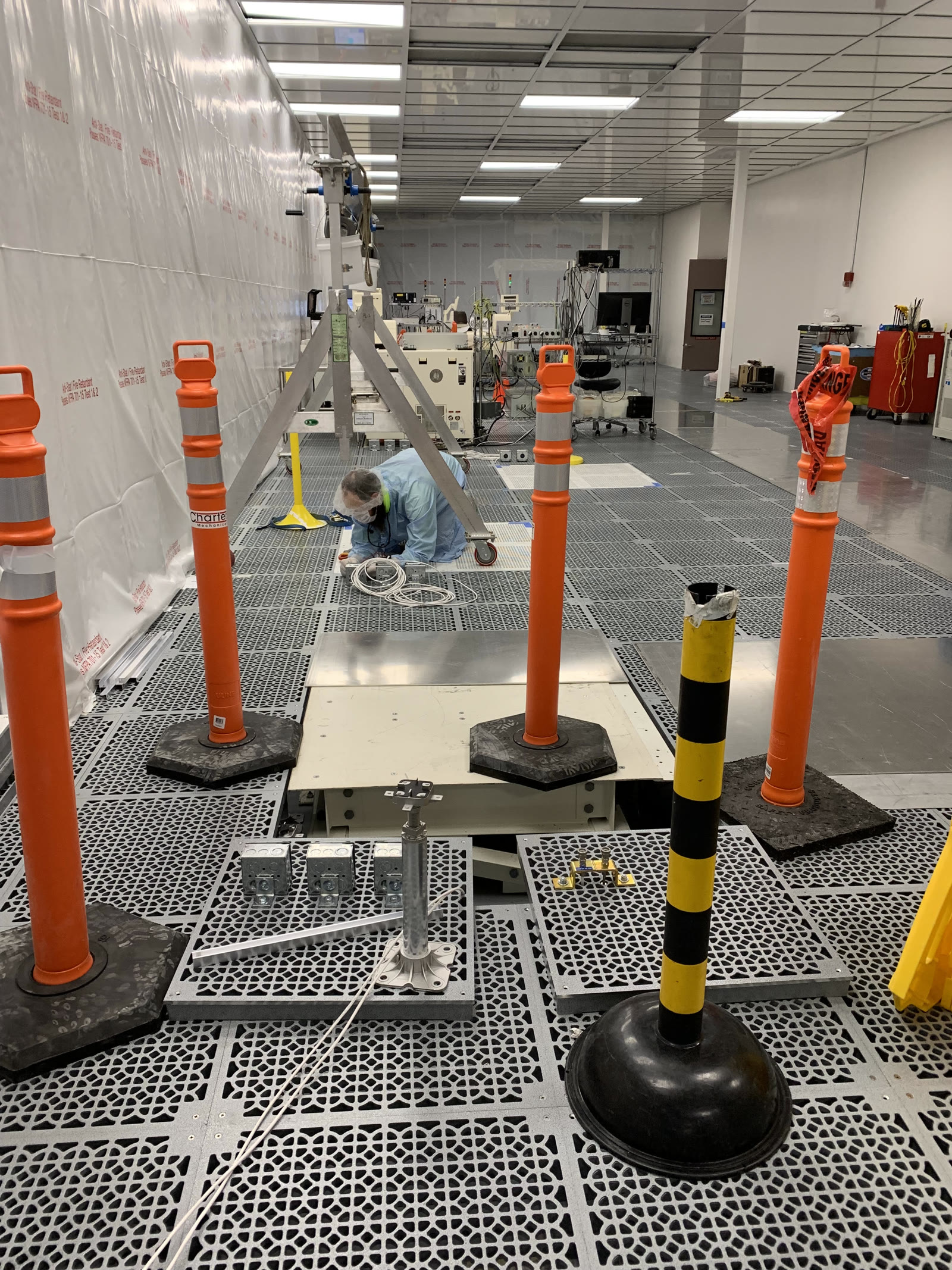 A technician in coveralls and a mask wiring floor boxes in a raised-access-floor cleanroom build-out